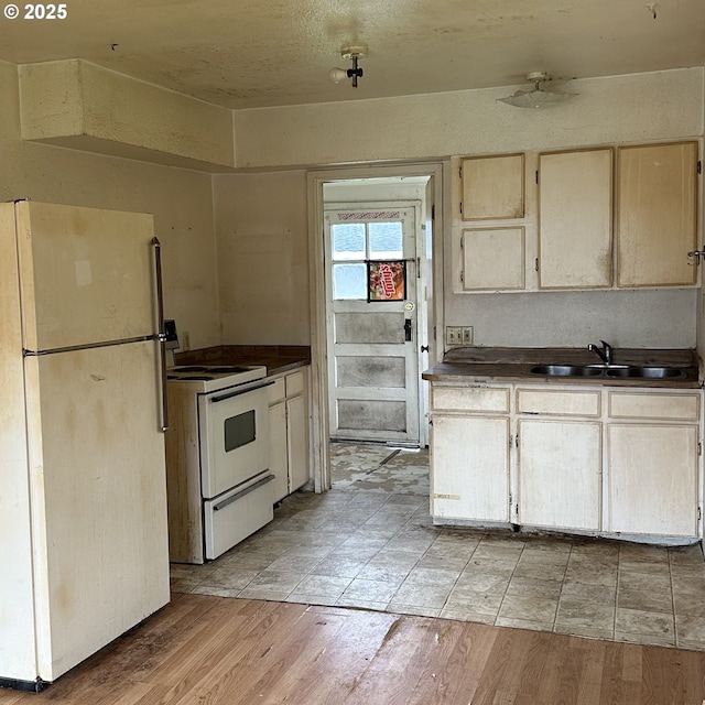 kitchen featuring dark countertops, light wood-style flooring, white appliances, and a sink