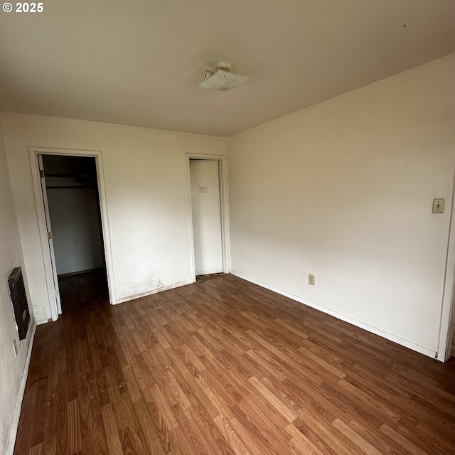 unfurnished bedroom with heating unit, wood finished floors, and a spacious closet