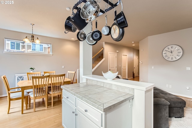 kitchen with decorative light fixtures, light hardwood / wood-style flooring, white cabinets, a chandelier, and tile counters