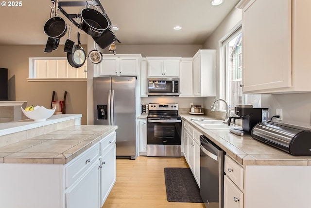 kitchen with appliances with stainless steel finishes, light wood-type flooring, sink, tile countertops, and white cabinets