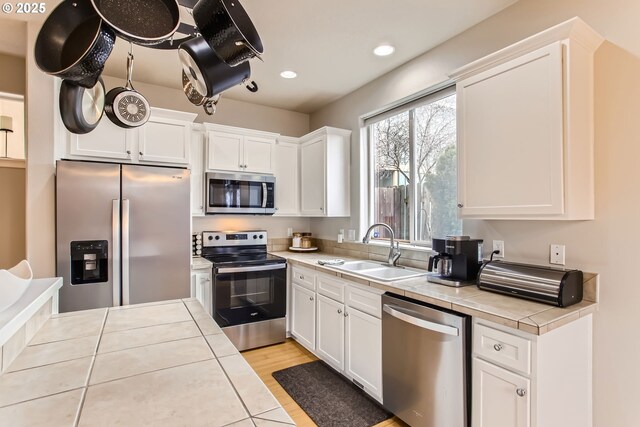 kitchen with appliances with stainless steel finishes, light wood-type flooring, sink, tile countertops, and white cabinets