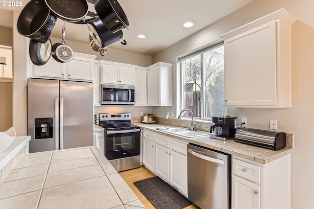 kitchen with tile countertops, white cabinets, sink, light wood-type flooring, and stainless steel appliances