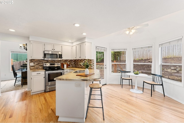 kitchen with light wood finished floors, a peninsula, a sink, stainless steel appliances, and backsplash