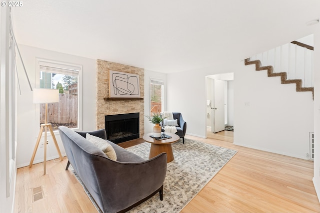 living room featuring a fireplace, visible vents, light wood finished floors, and baseboards