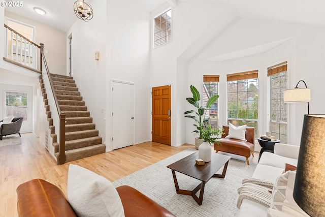 living room with a towering ceiling, a chandelier, light wood-style flooring, and stairs