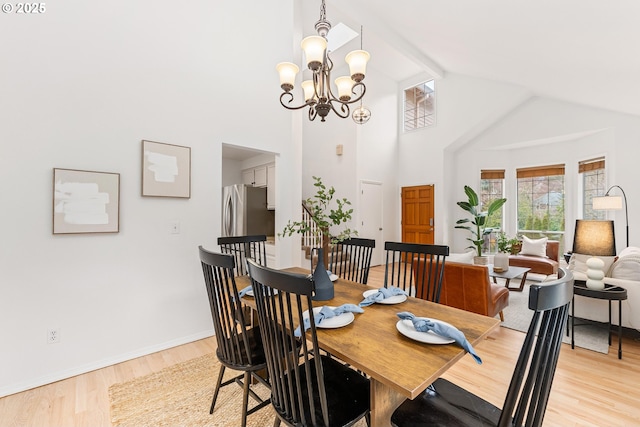 dining area featuring light wood finished floors, a chandelier, high vaulted ceiling, and baseboards