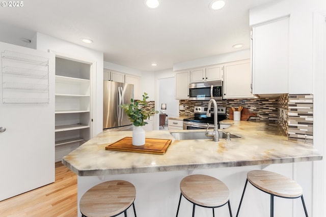 kitchen featuring backsplash, a breakfast bar, light countertops, appliances with stainless steel finishes, and a peninsula