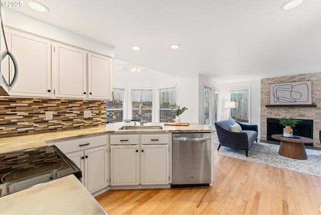 kitchen with white cabinetry, light countertops, dishwasher, open floor plan, and a large fireplace