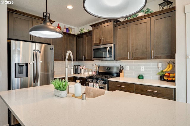 kitchen with dark brown cabinetry, pendant lighting, stainless steel appliances, and decorative backsplash