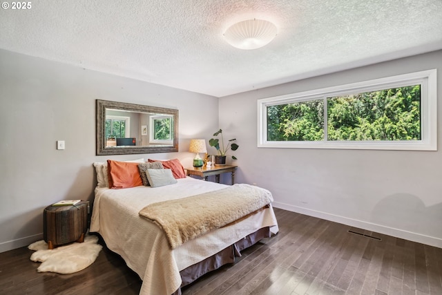 bedroom featuring baseboards, a textured ceiling, wood finished floors, and visible vents