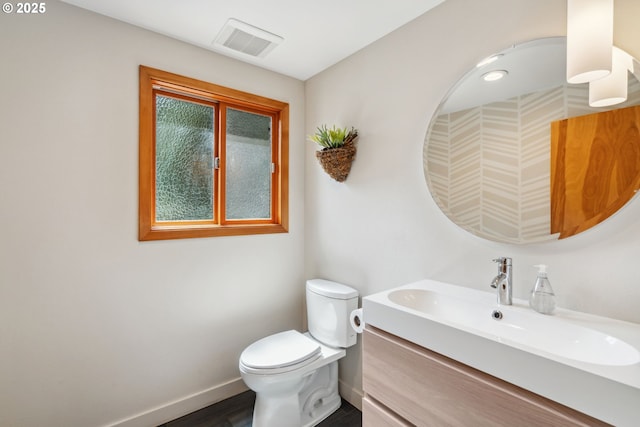 half bath featuring baseboards, vanity, toilet, and visible vents