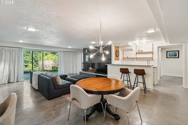 dining room with finished concrete floors, a textured ceiling, a notable chandelier, and a warm lit fireplace
