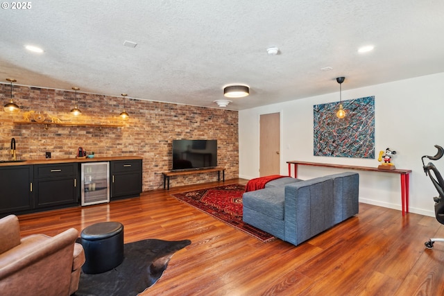 living room with beverage cooler, a textured ceiling, wood finished floors, and indoor wet bar