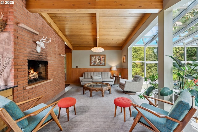 carpeted living room featuring wooden walls, a brick fireplace, a wainscoted wall, beamed ceiling, and wood ceiling