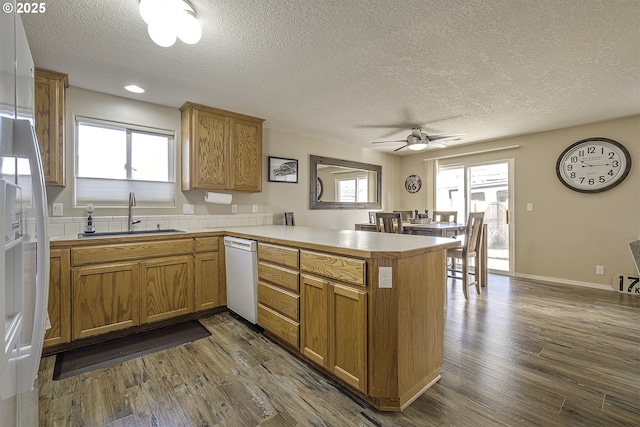 kitchen with kitchen peninsula, sink, white dishwasher, a textured ceiling, and dark wood-type flooring