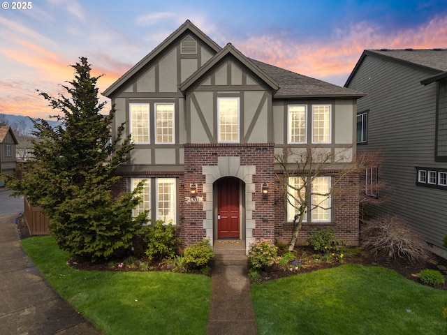 tudor house featuring a yard, roof with shingles, stucco siding, and brick siding