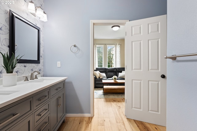 full bathroom featuring a sink, wood finished floors, double vanity, connected bathroom, and baseboards