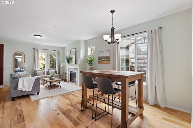 dining area with baseboards, a glass covered fireplace, light wood-type flooring, and a chandelier