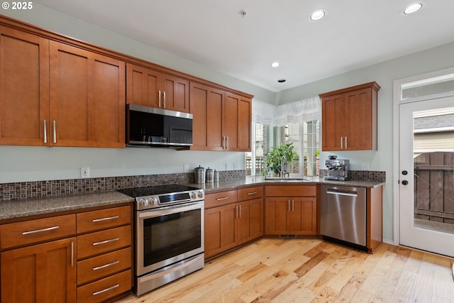 kitchen with a sink, brown cabinetry, stainless steel appliances, and light wood-style flooring