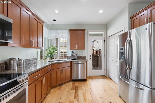 kitchen featuring light wood-style floors, dark stone countertops, appliances with stainless steel finishes, and a sink