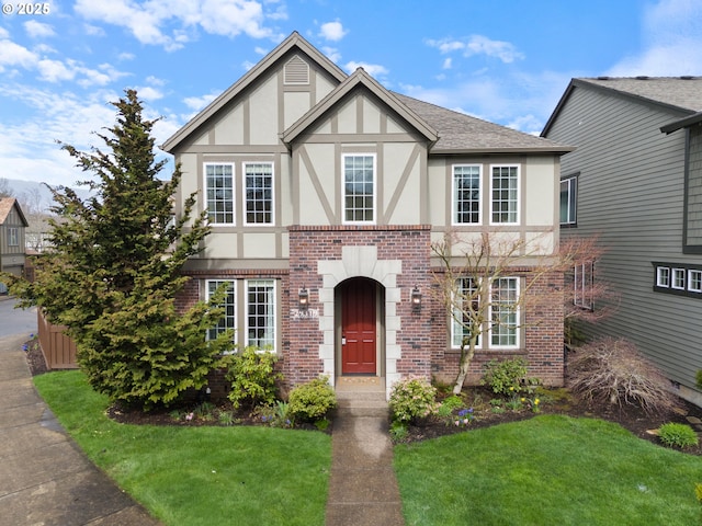 tudor-style house with brick siding, roof with shingles, stucco siding, and a front yard