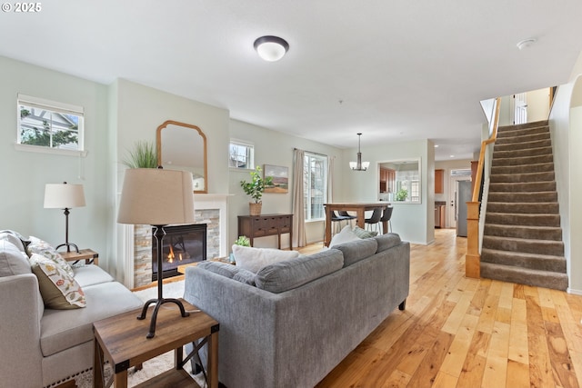 living room featuring a stone fireplace, light wood-style floors, a wealth of natural light, and stairway