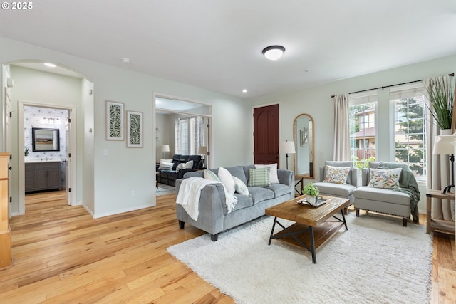 living area with arched walkways, baseboards, and light wood finished floors