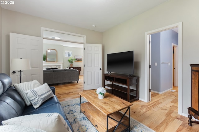 living room featuring a fireplace, baseboards, and light wood-style floors