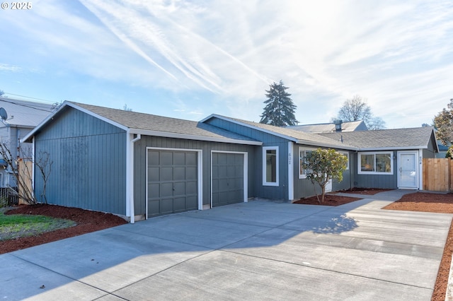 ranch-style home featuring concrete driveway, roof with shingles, fence, and an attached garage