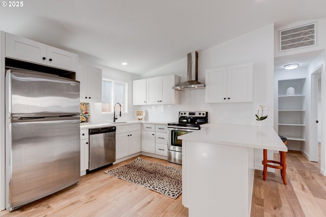 kitchen with a breakfast bar, stainless steel appliances, visible vents, a peninsula, and wall chimney exhaust hood