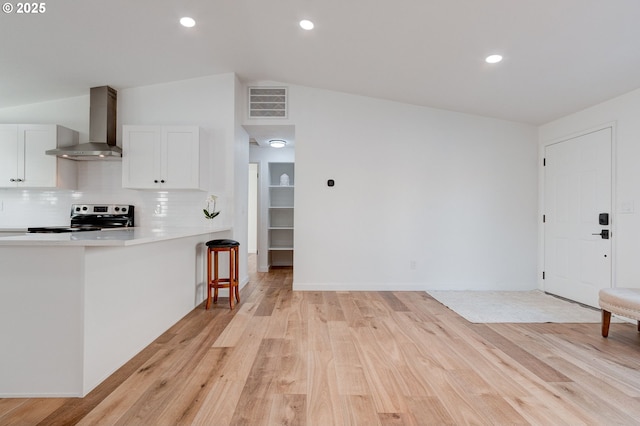 kitchen with white cabinets, light wood-style floors, wall chimney range hood, backsplash, and stainless steel electric stove