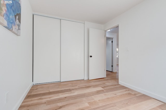 unfurnished bedroom with a closet, light wood-style flooring, and baseboards