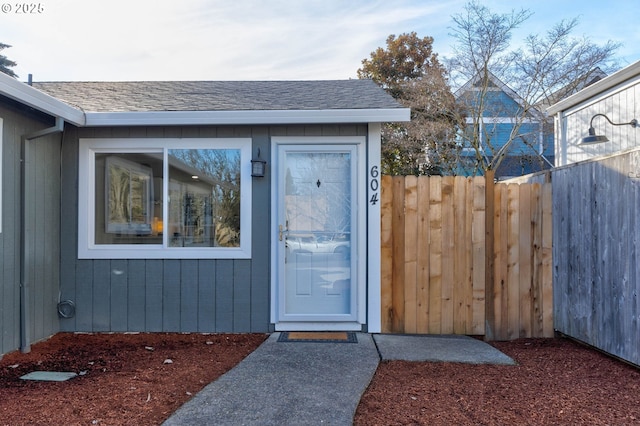 entrance to property featuring roof with shingles and fence