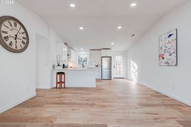 kitchen with a peninsula, light wood-style floors, white cabinets, and freestanding refrigerator