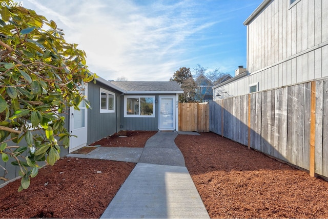 view of exterior entry featuring roof with shingles and fence