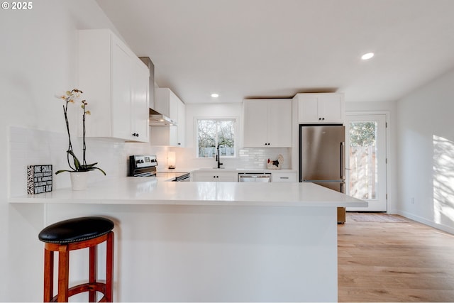 kitchen featuring appliances with stainless steel finishes, a peninsula, extractor fan, light countertops, and a sink