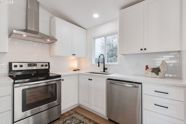 kitchen with wall chimney range hood, a sink, appliances with stainless steel finishes, and white cabinets