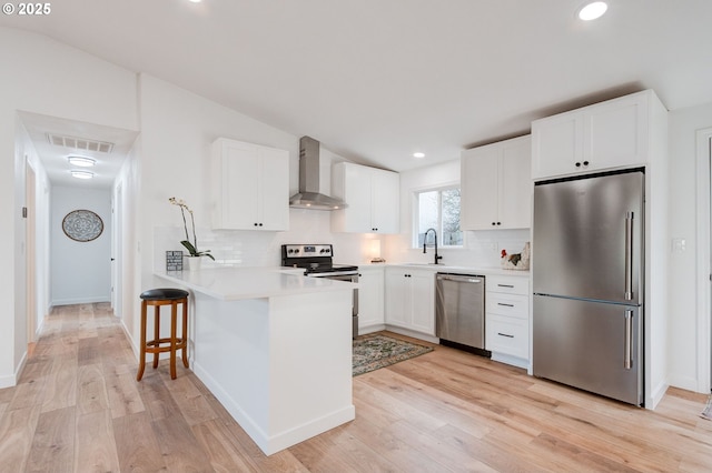 kitchen with visible vents, appliances with stainless steel finishes, a sink, a peninsula, and wall chimney exhaust hood