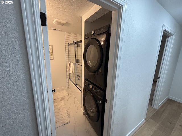 laundry room with laundry area, baseboards, marble finish floor, a textured ceiling, and stacked washing maching and dryer