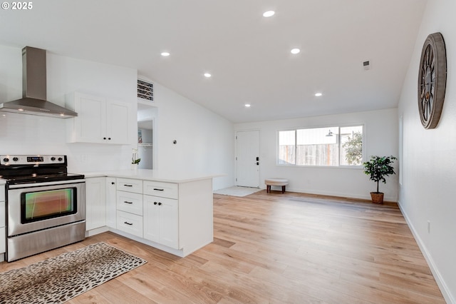 kitchen featuring white cabinets, lofted ceiling, wall chimney exhaust hood, stainless steel electric range oven, and a peninsula