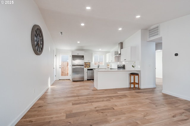 kitchen featuring light wood finished floors, visible vents, appliances with stainless steel finishes, white cabinets, and wall chimney range hood