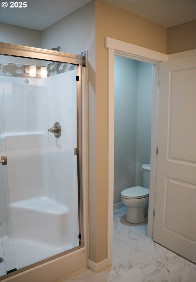 bathroom with toilet, marble finish floor, a shower stall, and baseboards