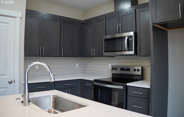 kitchen with light countertops, appliances with stainless steel finishes, a sink, and tasteful backsplash