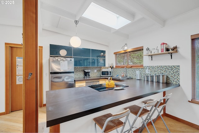 kitchen featuring backsplash, beam ceiling, a skylight, light wood-style floors, and stainless steel appliances