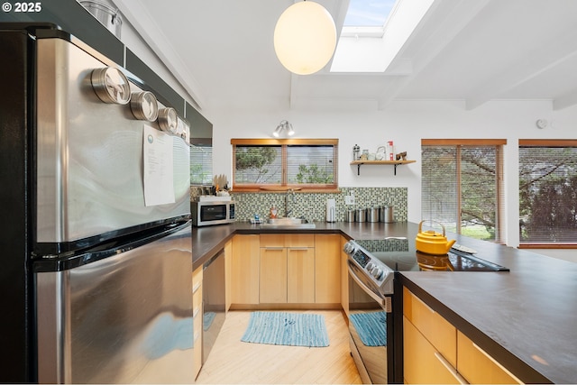 kitchen with beam ceiling, a sink, dark countertops, appliances with stainless steel finishes, and a skylight