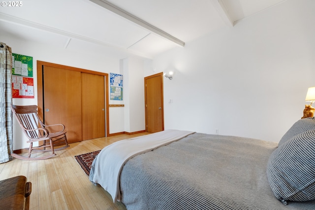 bedroom with beamed ceiling, wood finished floors, and a closet