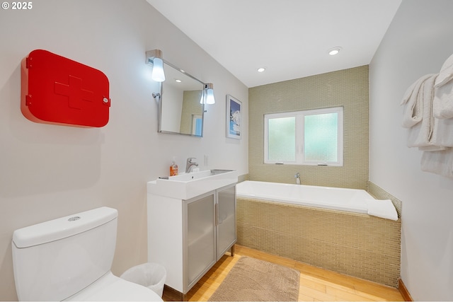 bathroom featuring toilet, wood finished floors, recessed lighting, a bath, and vanity