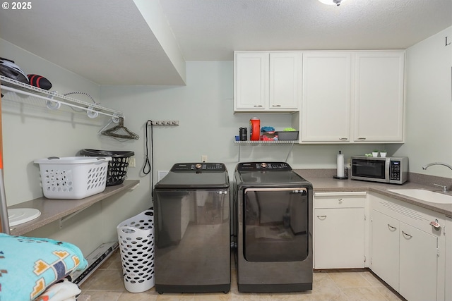 clothes washing area with washing machine and clothes dryer, light tile patterned floors, cabinet space, a sink, and a textured ceiling