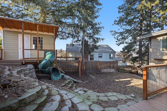 view of yard featuring a deck, a playground, and fence