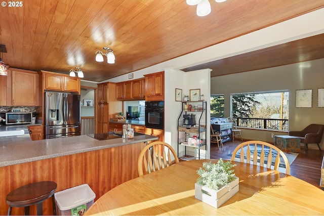 kitchen with brown cabinetry, wood finished floors, wooden ceiling, a peninsula, and black appliances